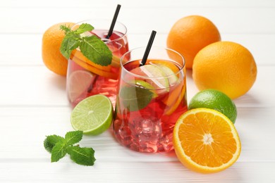 Photo of Tasty punch with ice, mint and slices of fruits in glasses on white wooden table, closeup. Refreshing drink