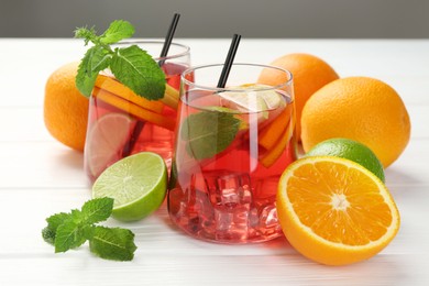 Photo of Tasty punch with ice, mint and slices of fruits in glasses on white wooden table against grey background, closeup. Refreshing drink