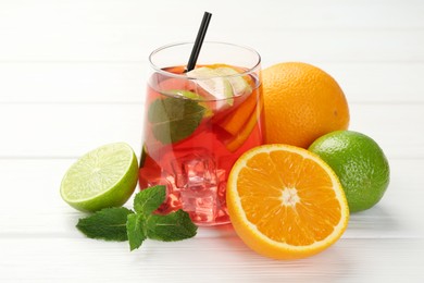 Photo of Tasty punch with ice, mint and slices of fruits in glass on white wooden table, closeup. Refreshing drink