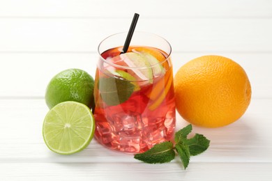 Photo of Tasty punch with ice, mint and slices of fruits in glass on white wooden table, closeup. Refreshing drink