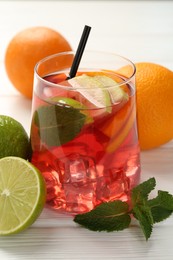 Photo of Tasty punch with ice, mint and slices of fruits in glass on white wooden table, closeup. Refreshing drink