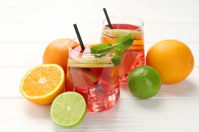 Photo of Tasty punch with ice, mint and slices of fruits in glasses on white wooden table, closeup. Refreshing drink