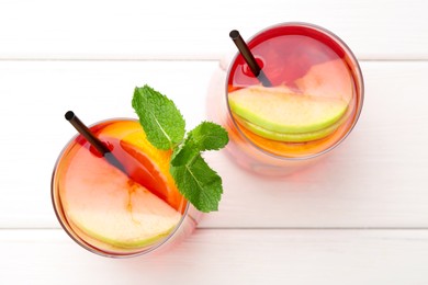 Photo of Tasty punch with mint and slices of fruits in glasses on white wooden table, flat lay. Refreshing drink