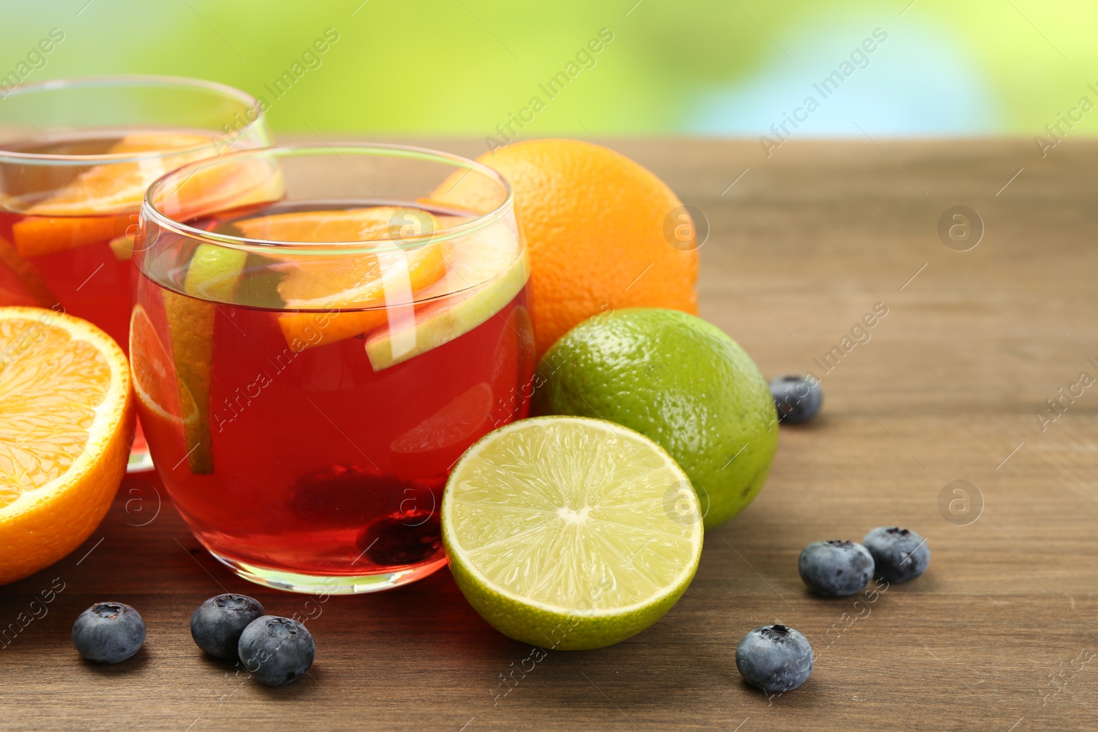 Photo of Tasty punch with fruits and blueberries on wooden table against blurred green background, closeup. Refreshing drink