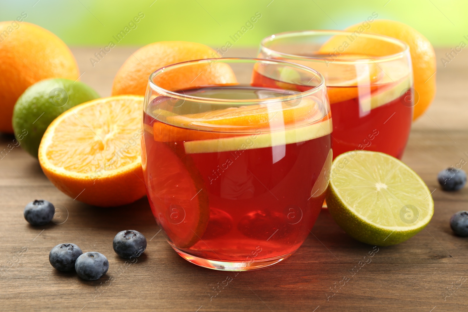 Tasty punch with fruits and blueberries on wooden table against blurred green background, closeup. Refreshing drink Photo of Tasty punch with fruits and blueberries on wooden table against blurred green background, closeup. Refreshing drink