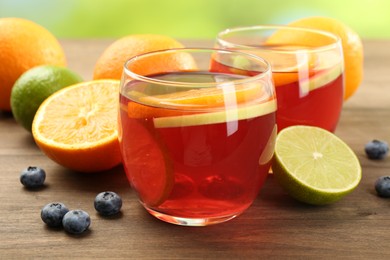 Photo of Tasty punch with fruits and blueberries on wooden table against blurred green background, closeup. Refreshing drink