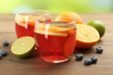 Photo of Tasty punch with fruits and blueberries on wooden table against blurred green background, closeup. Refreshing drink