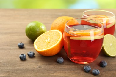 Photo of Tasty punch with fruits and blueberries on wooden table against blurred green background, closeup. Refreshing drink