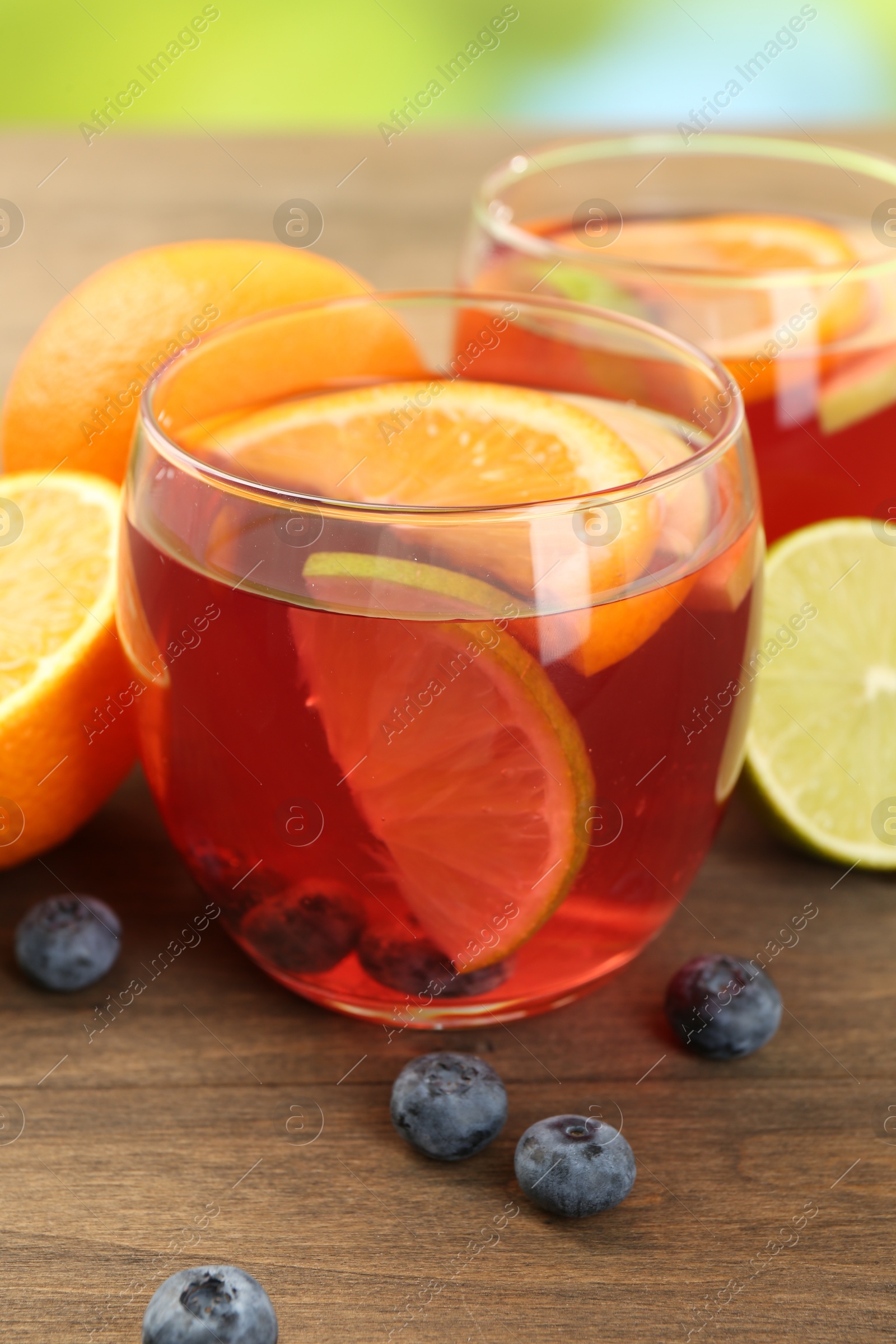 Photo of Tasty punch with fruits and blueberries on wooden table against blurred green background, closeup. Refreshing drink