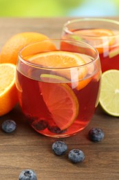 Photo of Tasty punch with fruits and blueberries on wooden table against blurred green background, closeup. Refreshing drink