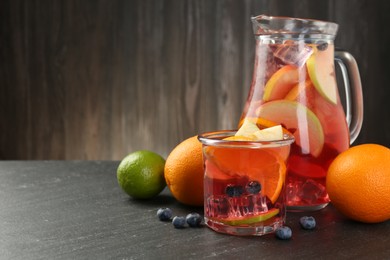 Photo of Tasty punch, fruits and berries on dark gray textured table. Space for text