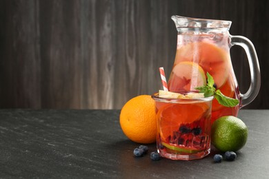 Photo of Tasty punch, fruits and berries on dark gray textured table. Space for text