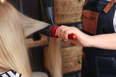 Photo of Hairstylist blow drying client's hair in salon, closeup