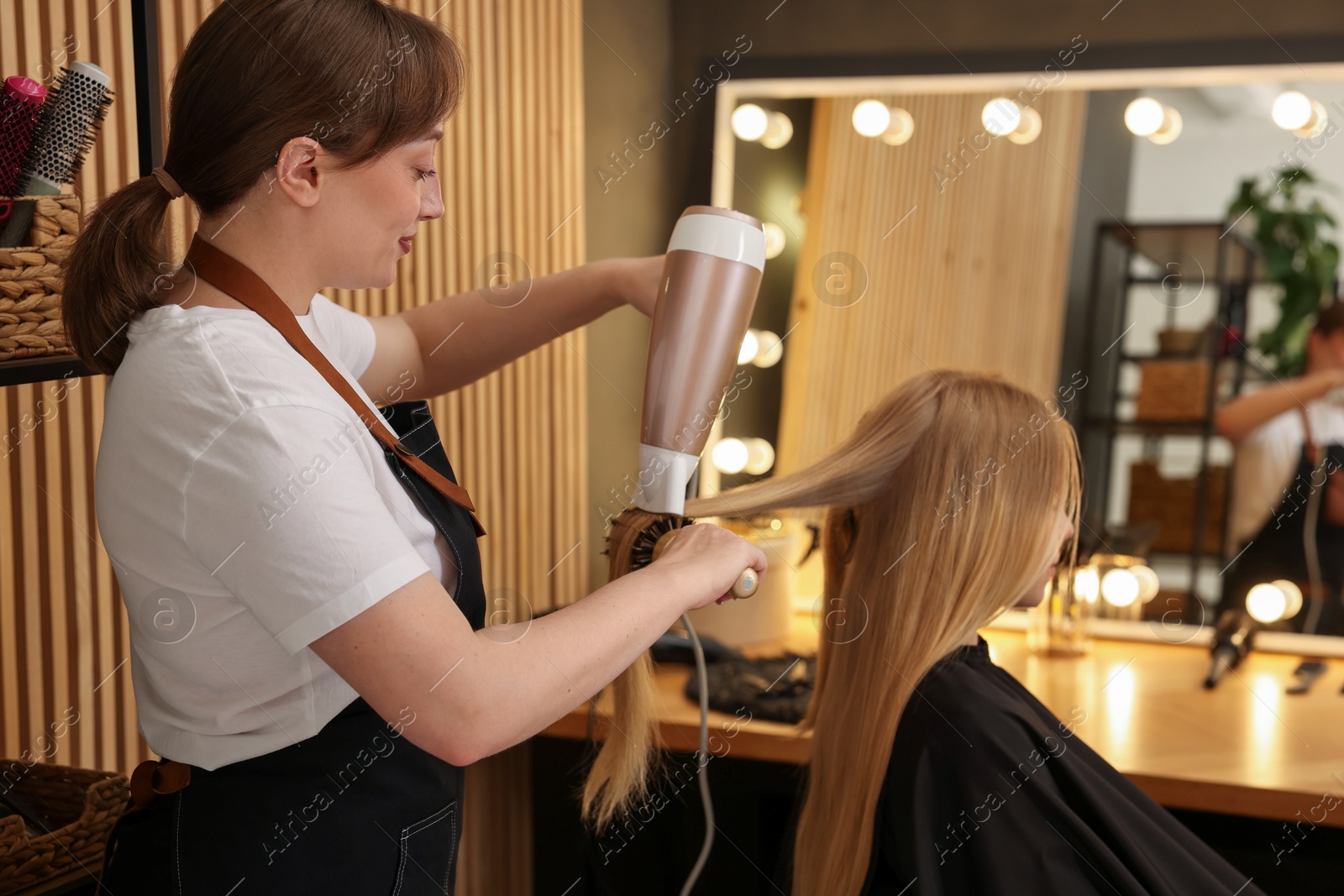 Hairstylist blow drying client's hair in salon Photo of Hairstylist blow drying client's hair in salon