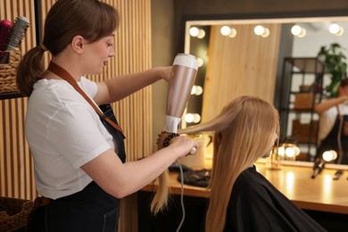 Photo of Hairstylist blow drying client's hair in salon