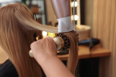 Photo of Hairstylist blow drying client's hair in salon, closeup