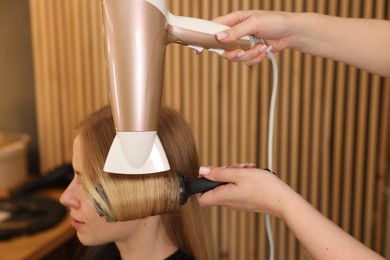 Photo of Hairstylist blow drying client's hair in salon, closeup