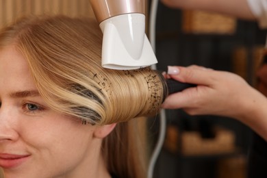 Photo of Hairstylist blow drying client's hair in salon, closeup