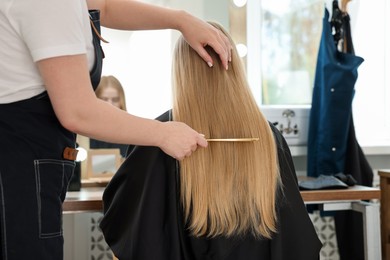 Photo of Professional hairstylist combing woman's hair in salon, closeup