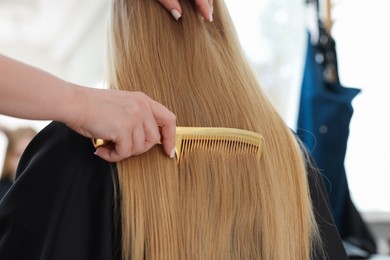 Photo of Professional hairstylist combing woman's hair in salon, closeup