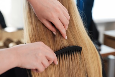 Photo of Professional hairstylist combing woman's hair in salon, closeup