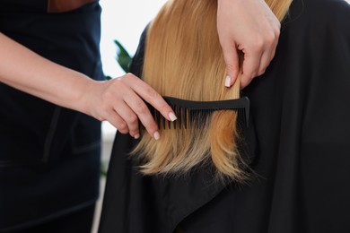 Photo of Professional hairstylist combing woman's hair in salon, closeup