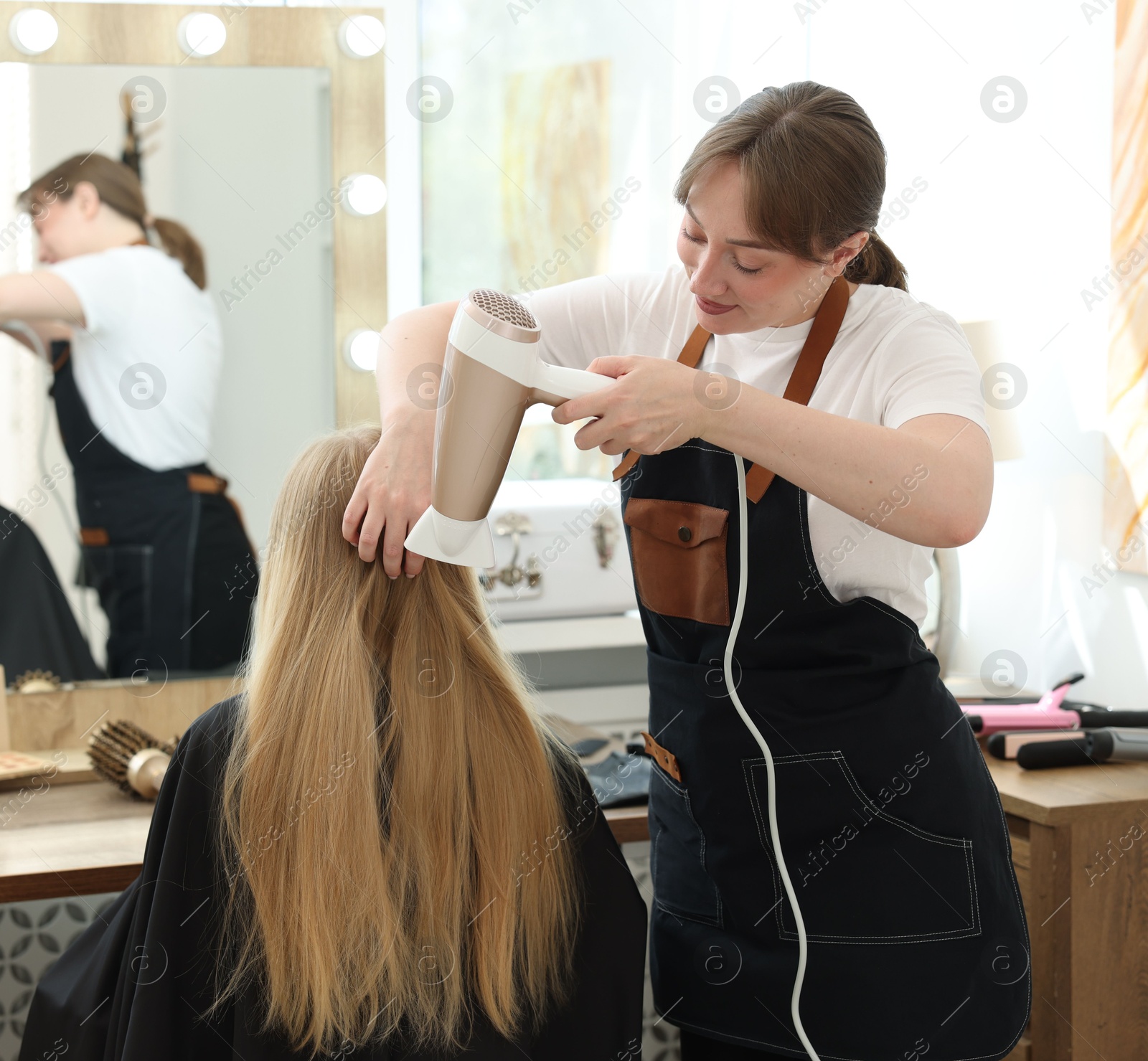 Hairstylist blow drying client's hair in salon Photo of Hairstylist blow drying client's hair in salon