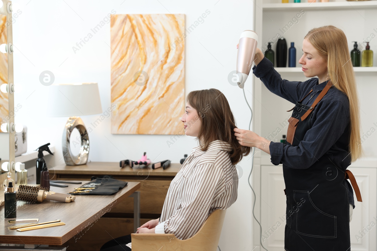 Hairstylist blow drying client's hair in salon Photo of Hairstylist blow drying client's hair in salon