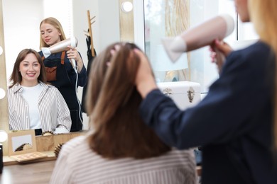 Photo of Hairstylist blow drying client's hair in salon, closeup