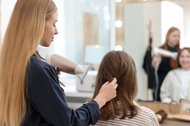 Photo of Hairstylist blow drying client's hair in salon