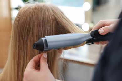Photo of Hairstylist curling woman's hair in salon, closeup
