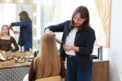 Photo of Professional hairstylist curling woman's hair in salon