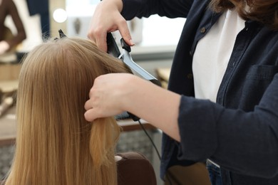 Photo of Professional hairstylist curling woman's hair in salon, closeup