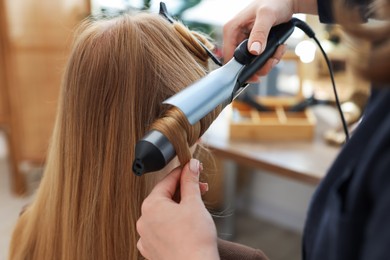 Photo of Professional hairstylist curling woman's hair in salon, closeup