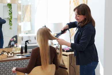 Photo of Professional hairstylist curling woman's hair in salon