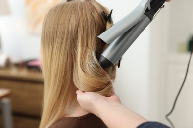 Photo of Professional hairstylist curling woman's hair in salon, closeup