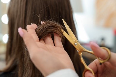 Photo of Hairstylist cutting client's hair with scissors in salon, closeup