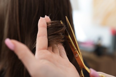 Photo of Hairstylist cutting client's hair with scissors in salon, closeup