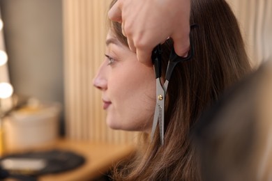 Photo of Hairstylist cutting client's hair with scissors in salon, closeup