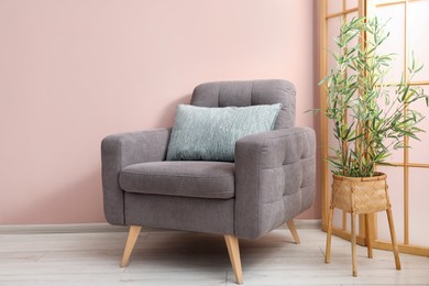 Photo of Comfortable armchair with cushion and houseplant near beige wall indoors