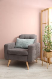Photo of Comfortable armchair with cushion and houseplant near beige wall indoors