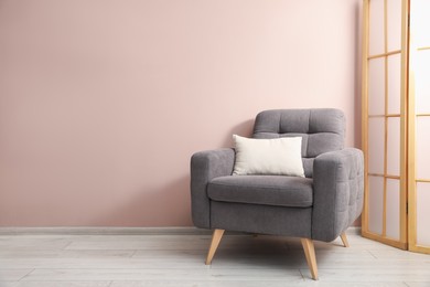 Photo of Comfortable armchair and cushion near beige wall indoors. Space for text