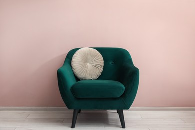 Photo of Comfortable armchair and cushion near beige wall indoors