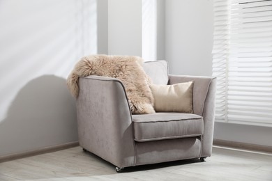 Photo of Comfortable armchair, fluffy blanket and cushion in light room