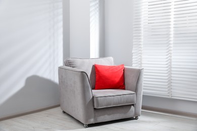 Photo of Comfortable armchair and red cushion near window in light room