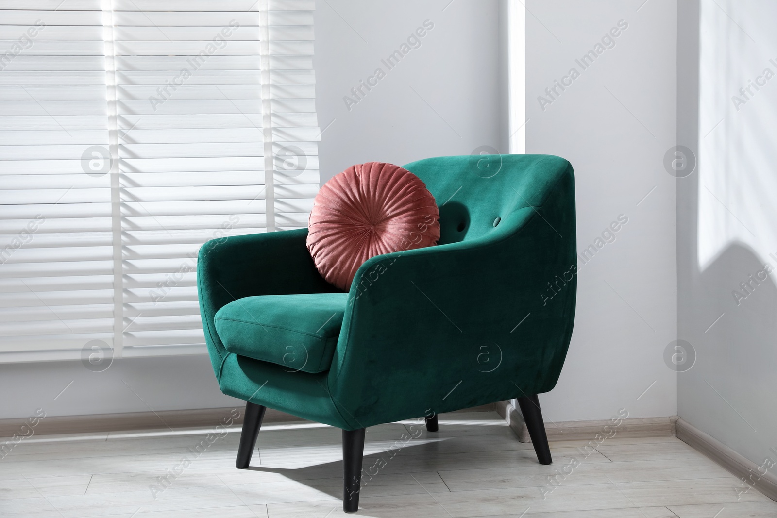 Photo of Comfortable armchair and cushion near window in light room