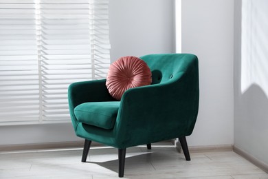 Photo of Comfortable armchair and cushion near window in light room