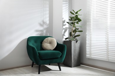 Photo of Comfortable armchair with cushion and houseplant near window in light room