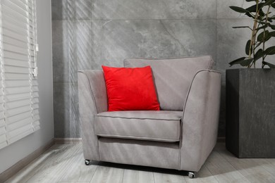 Photo of Comfortable armchair, red cushion and houseplant near gray marble wall