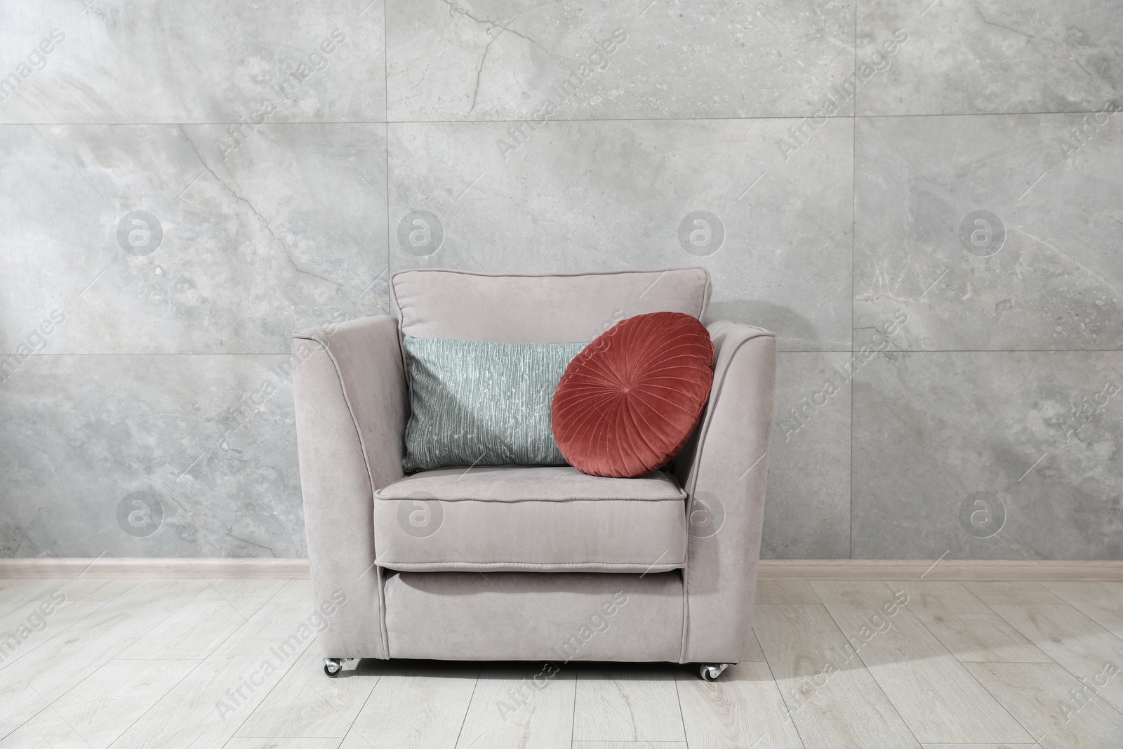 Photo of Comfortable armchair and cushions near gray marble wall